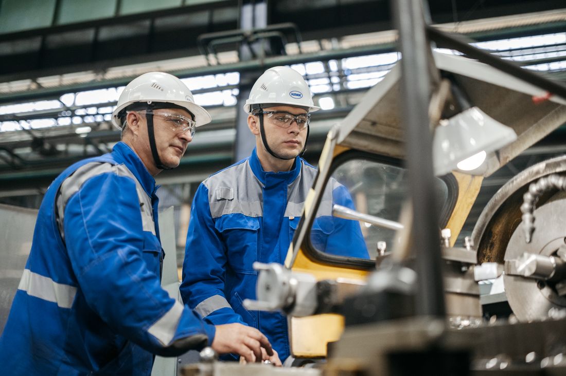 Zwei Montagekräfte mit Schutzhelmen arbeiten an einer Maschine in der Werkshalle